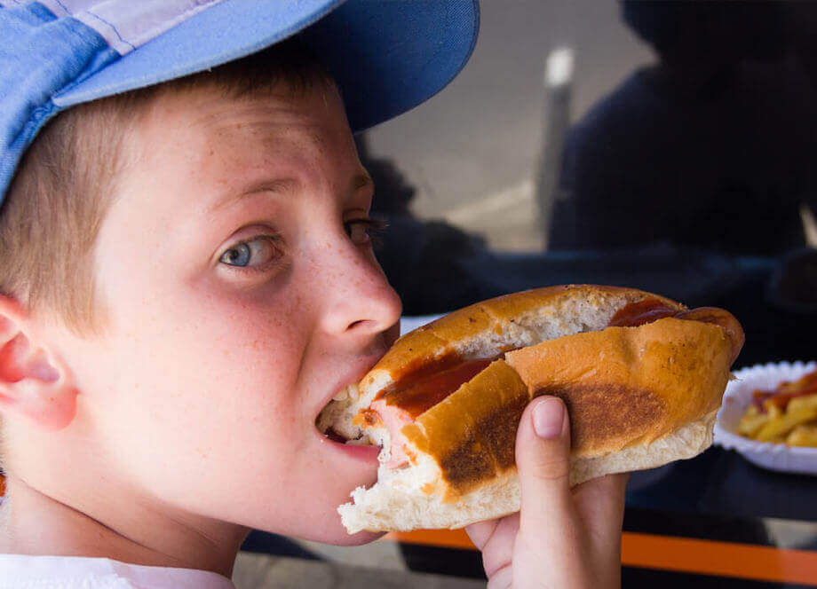 Boy with a blue hat eating a hot dog