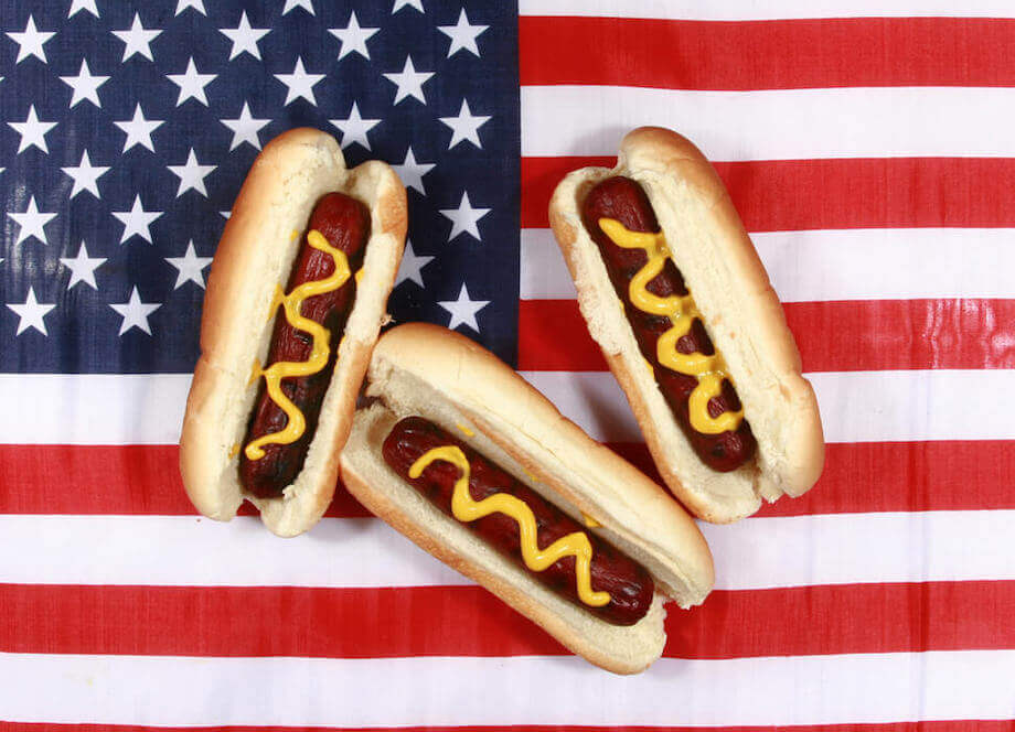 Three hot dogs with mustard sitting on an american flag