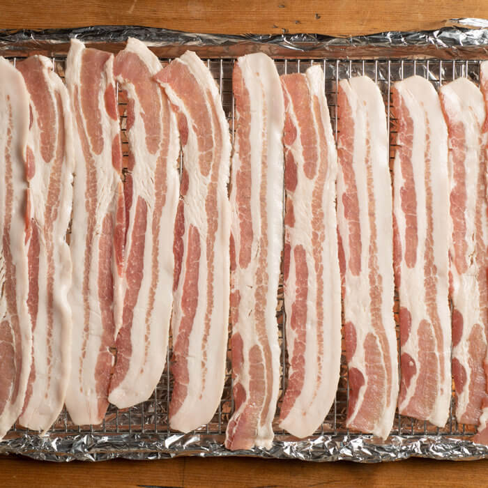 uncooked baccon on a foil lined cooking rack