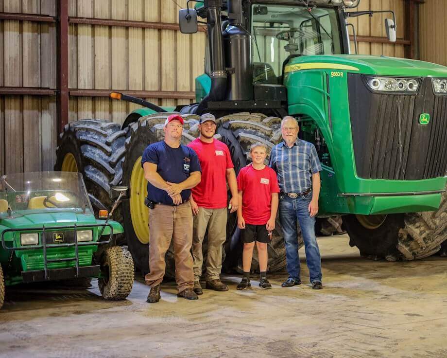 three farmers standing in front of farm equipment