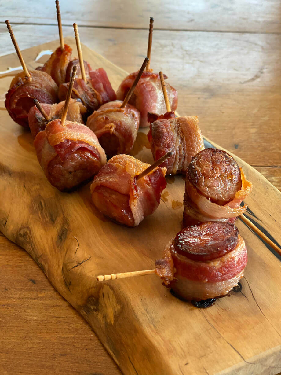 Bacon wrapped brat bites on a wooden serving board