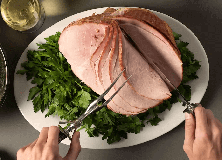 hands slicing spiral ham on a white plate