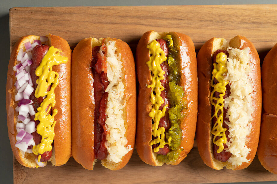 four hot dogs dressed and lined up on a wooden plate