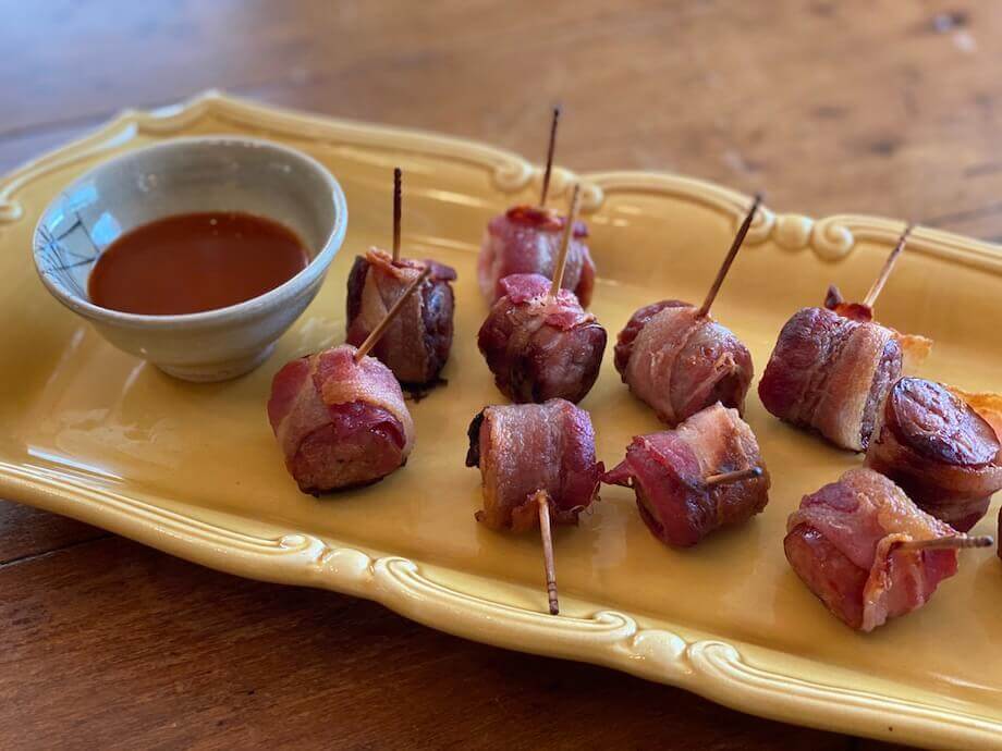 Bacon wrapped brat bites on a yellow plate with hot sauce