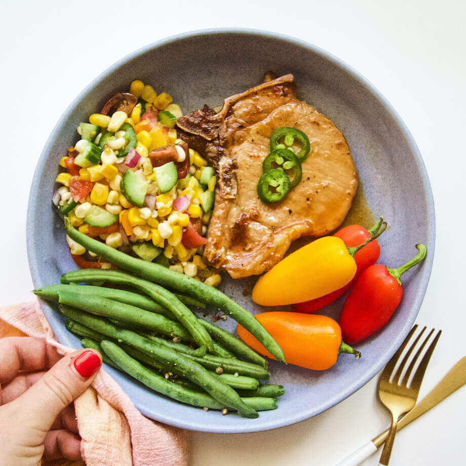 Honey hot chops with corn, peppers, and green beans on a grey plate