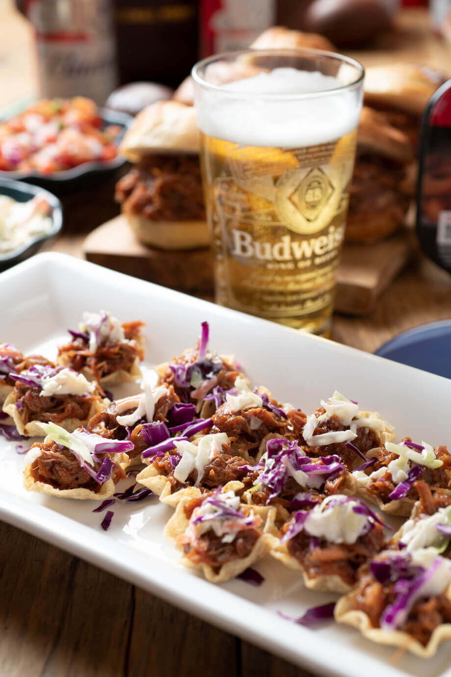 Pulled pork bites on a white serving plate next to a glass of beer