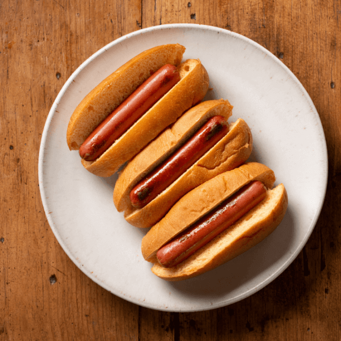 Three hot dogs in buns sitting on a white plate