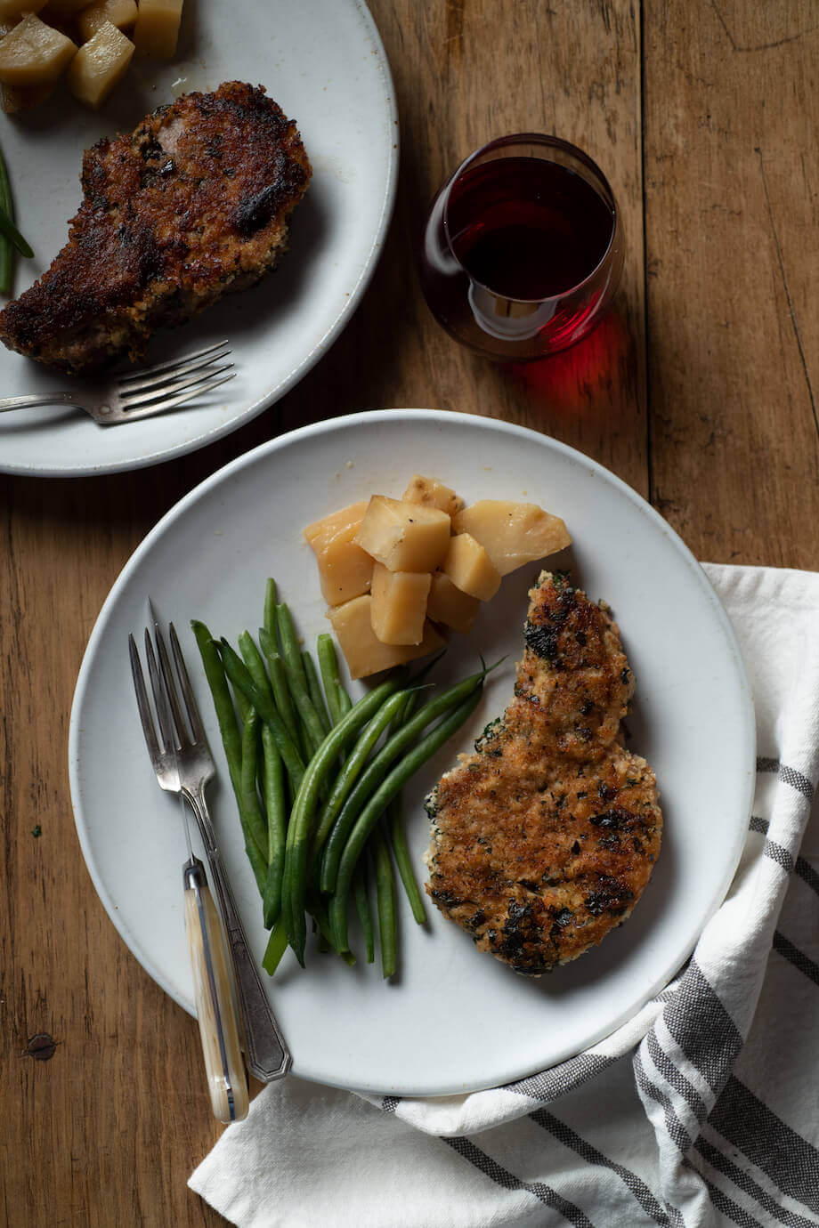 Herb crusted porkchop on a white plate with potatoes and green beans