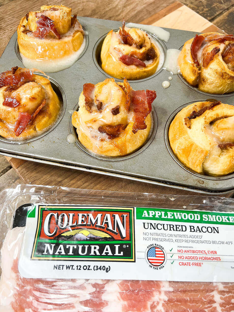 Maple bacon cinnamon rolls in a pan next to a package of applewood bacon