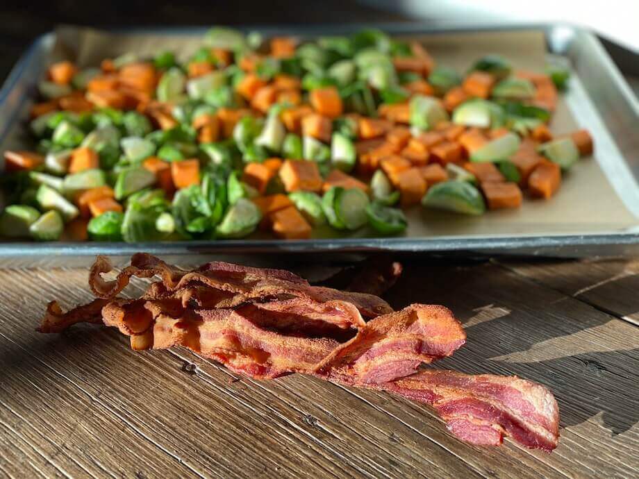 Carrots and brussel sprouts on a tray next to bacon