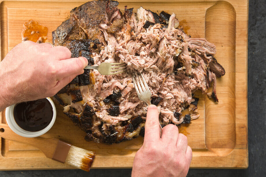 Hands using two forks to shred cooked pork