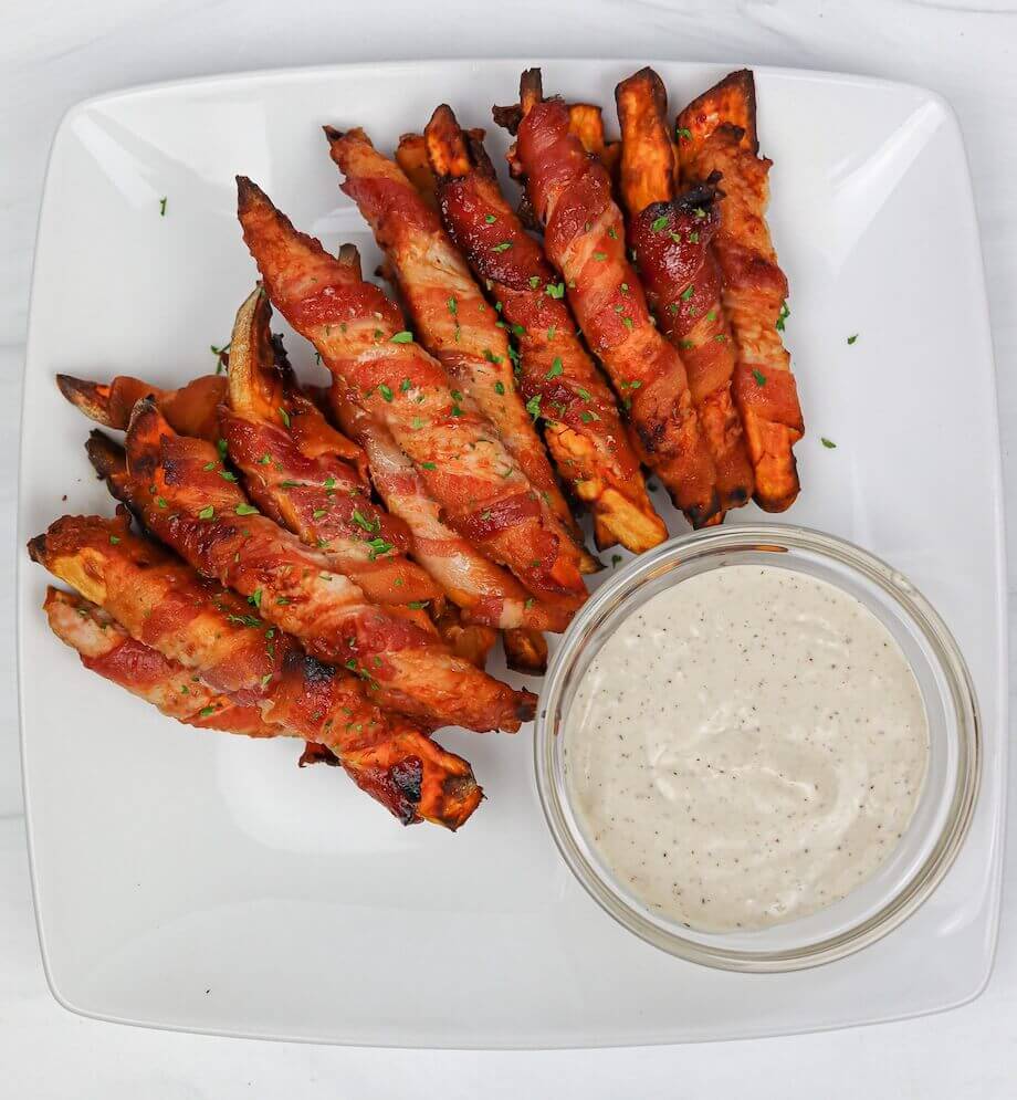 Bacon wrapped sweet potatoes with dipping sauce on a white plate