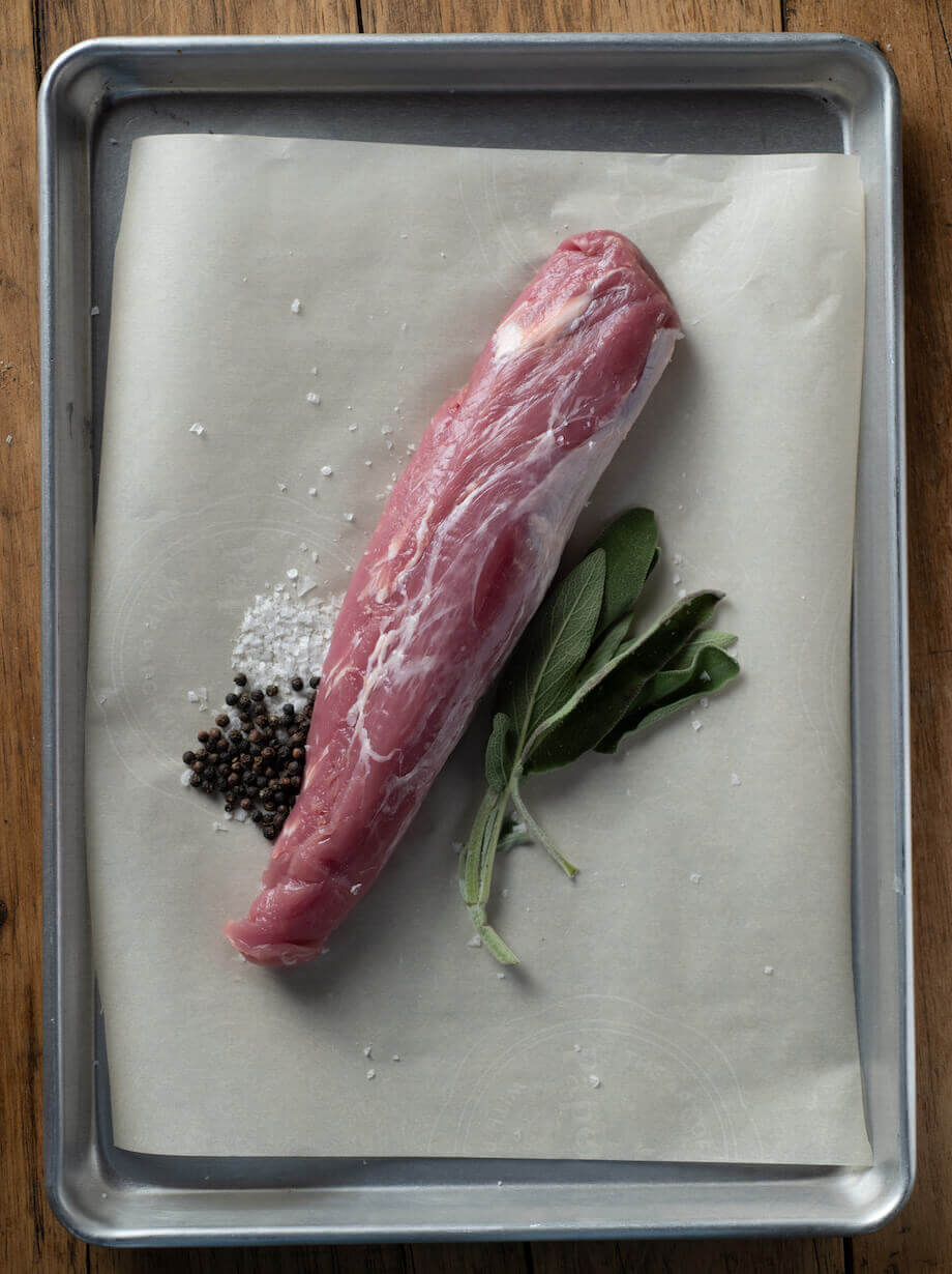 Raw pork loin on a baking sheet with salt and pepper