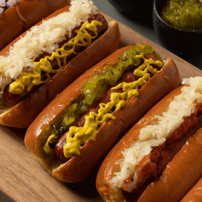 Row of hot dogs topped with mustard and relish on a wooden board