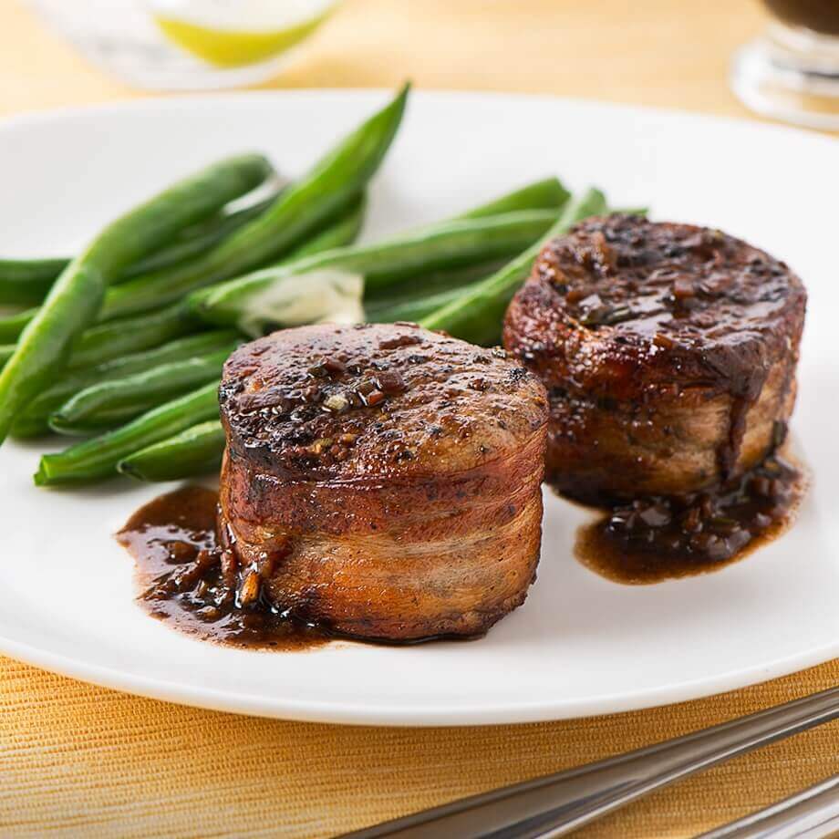 Bacon wrapped peppercorn pork tenderloin medallions on a white plate with green beans