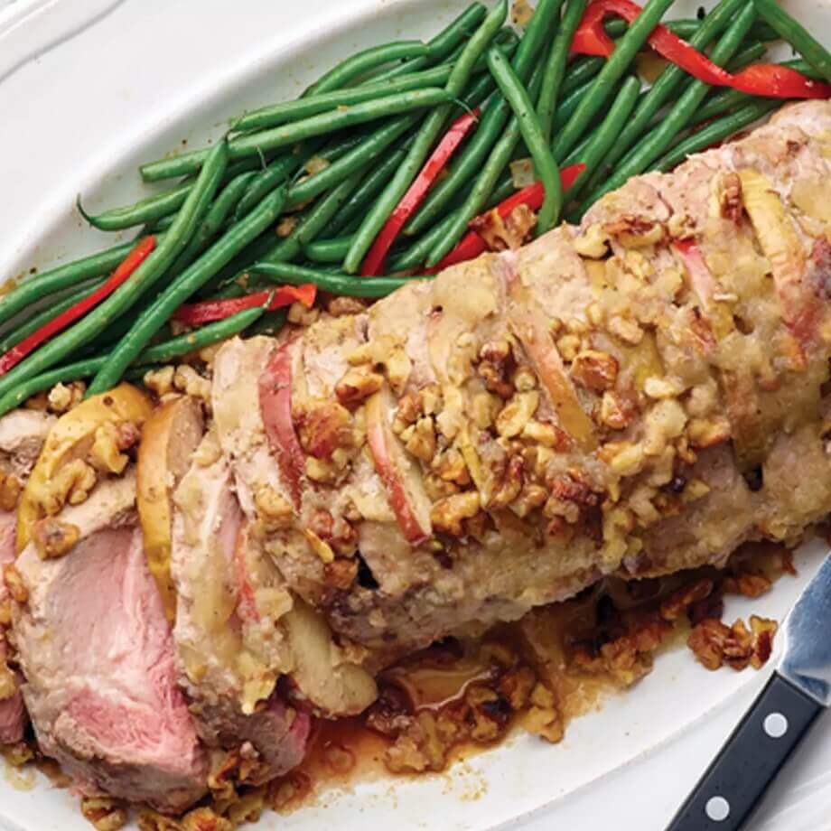 Paleo-friendly Hasselback Pork Tenderloin with Apples and Walnuts on a white plate with green beans